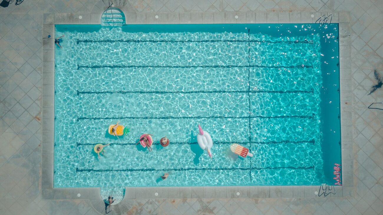 Top-down view of a swimming pool with colorful floats and people enjoying a sunny pool party.
