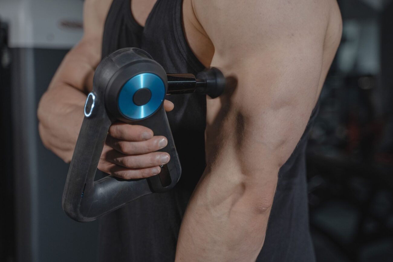 Close-up of a man using a massage gun for muscle relaxation on his arm.